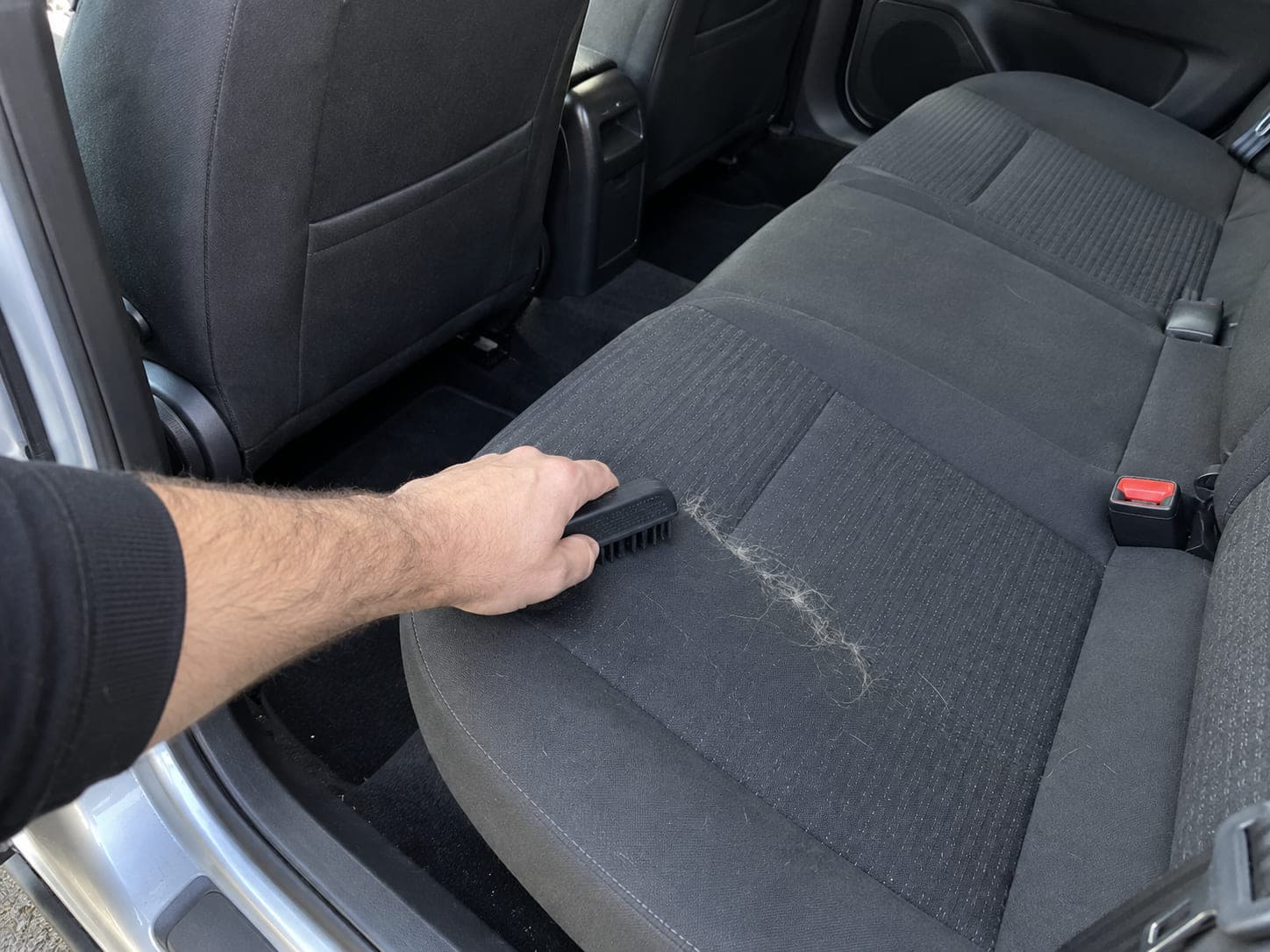 An illustration of pet hair being lifted from a vehicle seat with a rubber tool