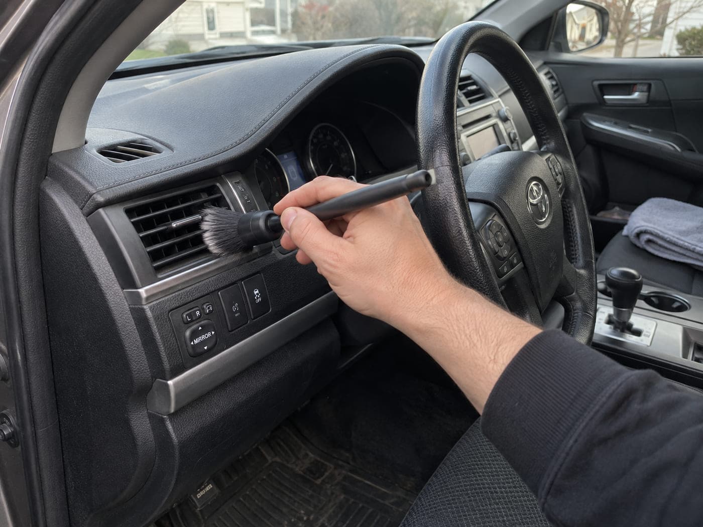 An illustration of a vehicle air vent being cleaned with a detailing brush