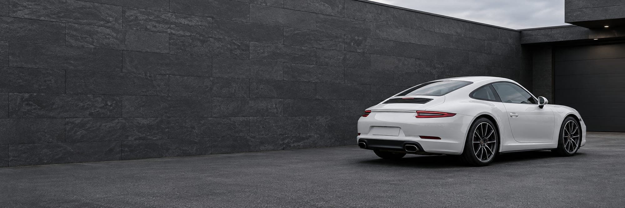 The front of a white sports car against a dark stone wall, headlights in shadow